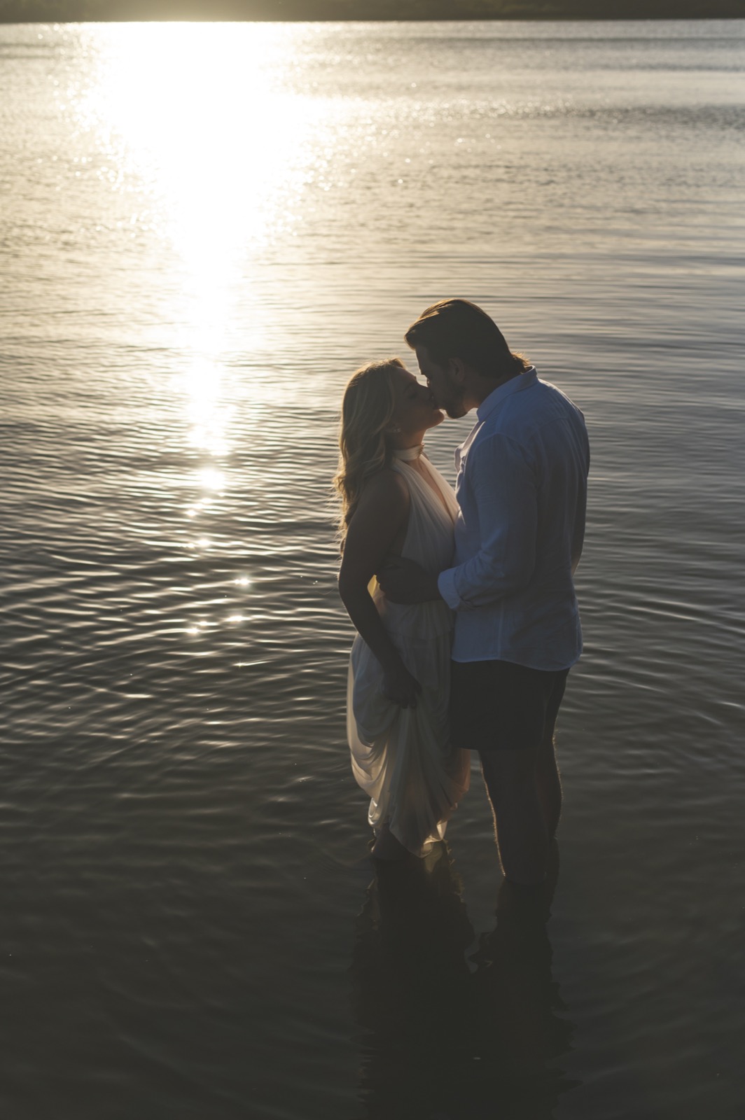 Casal em silhueta na água, se beijando, sol baixo
