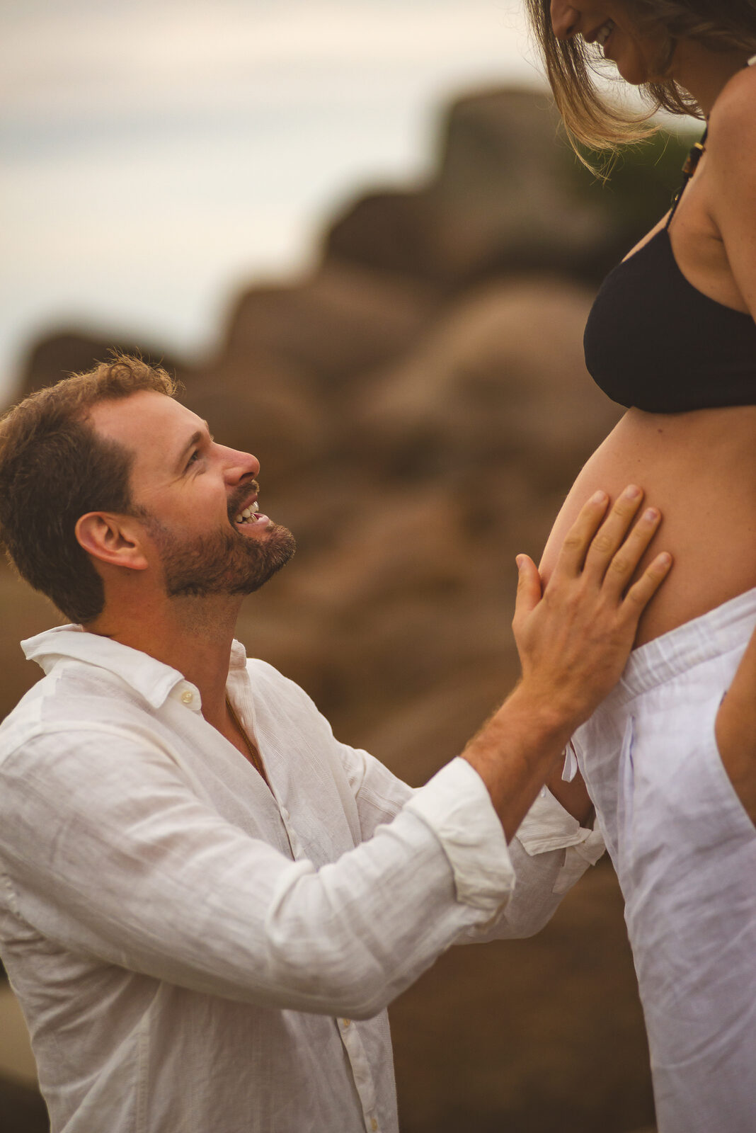 Ele ajoelhado com as mãos na barriga dela, rindo